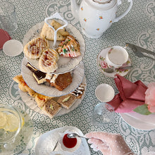 Load image into Gallery viewer, Tea party setup with pastries, teapot, and tea cups on a patterned tablecloth.