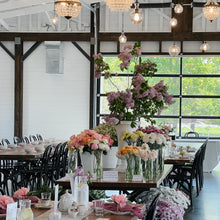 Load image into Gallery viewer, Elegant dining room with floral centerpieces and chandelier lights.
